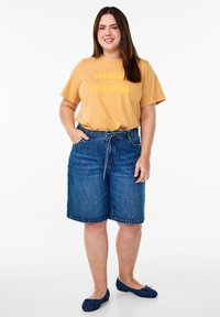 Shorts de mezclilla azul oscuro con un ajuste relajado, que cuentan con una cintura con cordón y bolsillos laterales. Combinados con una camiseta de manga corta color mostaza.