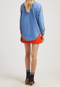 Jeansskjorta i ljusblått med lång ärm, rundad fåll och bakstycke. Matchad med en lysande orange minikjol och svarta ankelboots.
