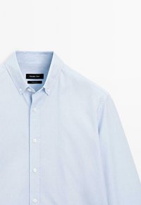 Lichtblauw overhemden met knoopsluiting en knoop-down kraag, met witte knopen, gelabeld Massimo Dutti, gemaakt in Turkije, weergegeven op een witte achtergrond.