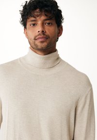 Maglione a collo alto beige realizzato in morbido materiale a maglia, con colletto aderente e vestibilità leggermente rilassata, caratterizzato da una consistenza liscia.
