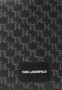 Juoda tekstūruota rankinė su embosiuotu geometriniu raštu ir logotipu "KARL LAGERFELD" juodame odiniame ženkle.