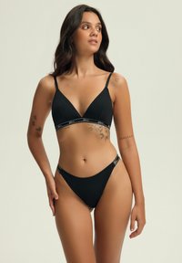 Black bikini set featuring a ribbed texture, triangular bralette with adjustable straps, and thin side bands. Notable floral and text accents.