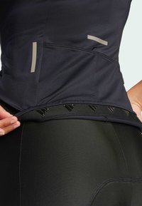 Czarna sportowa koszulka z odblaskowymi akcentami, teksturowanym materiałem i regulowanym dołem. W połączeniu z eleganckimi czarnymi legginsami, które podkreślają gładkie linie i minimalistyczny design.