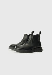 Bottes Chelsea en cuir noir avec une finition lisse, panneaux latéraux en élastique, languettes de tirage et semelles en caoutchouc épaises pour une meilleure adhérence.
