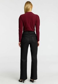 Bordeaux långärmad topp med texturerad tyg och dragkedja i ryggen, i kombination med högmidjade svarta utsvängda jeans. Svarta klackskor fulländar looken.