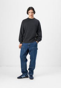 Svart hettegenser med rund hals, kombinert med løse blå denimjeans. Modellen har på seg mørkeblå sneakers med tre hvite striper.