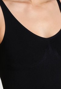 Débardeur noir en tissu extensible, avec un décolleté en forme de coeur, des accents texturés le long du centre et des bords lisses.