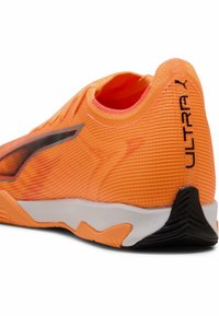 Scarpa sportiva arancione con superficie testurizzata, accenti neri a contrasto e suola bianca. Presenta un profilo basso e un design elegante.