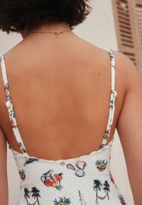 Vestido blanco con estampado floral, con tirantes finos, tela texturizada y botones decorativos en la parte trasera. Piel suave visible.