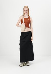Top corto marrón, falda larga negra con bolsillos, bolso cruzado beige y zapatillas grises. Diseño sencillo con estilo casual.