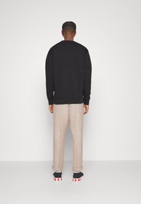 Svart sweatshirt med rundad halsringning, matchad med rutiga byxor med röda och beige rutor, samt svarta skor med röda detaljer.