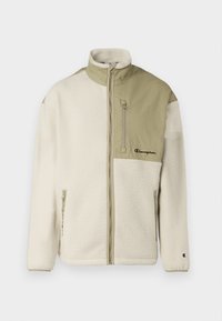 Chaqueta de forro polar con cuerpo crema y sección superior en verde oliva, cuello alto, bolsillo con cremallera en el pecho y logotipo bordado en el lado izquierdo.
