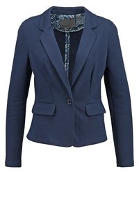 Blazer bleu marine en tissu lisse, présentant une coupe ajustée, des revers à cran, deux poches avant et une doublure intérieure à motif.