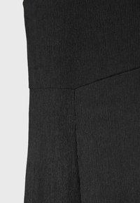 Gros plan sur un tissu noir texturé avec une couture visible traversant le matériau en diagonale, mettant en évidence la structure et la couture.