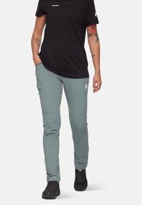 Pantalons de yoga gris avec une coupe slim, dotés de poches latérales, de coutures au niveau des genoux et d'une marque discrète, associés à un t-shirt noir à manches courtes.