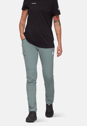 Graue Stretchpants inSlim Fit, ausgestattet mit seitlichen Taschen, Kniefalten und subtilen Branding, kombiniert mit einem schwarzen kurzärmeligen Shirt.