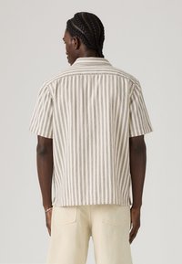 Short-sleeve shirt in cream with vertical navy stripes, button-down collar, and straight hem. Made of lightweight, textured fabric.