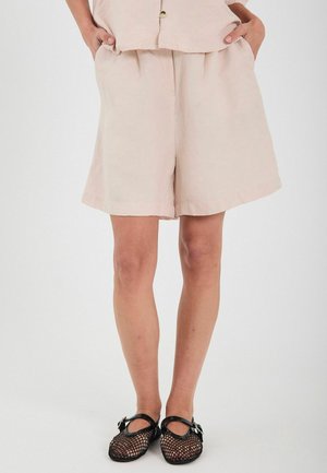 Svetloružové ľanové šortky s voľným strihom, s plisovaním a bočnými vreckami, v kombinácii s čiernymi sieťovanými topánkami. Hladká textúra, jednoduchý dizajn.