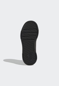 Semelle de chaussure en caoutchouc noir avec un motif hexagonal texturé, présentant des bords striés et le logo Adidas à la base.