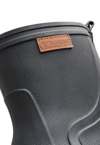 Botte en caoutchouc noire avec une surface texturée, un design courbé et une étiquette en cuir tan avec "hummel" embossé. Matériau durable et étanche.