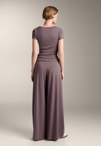 Mauve top z kratkimi rokavi, prilega se v pasu, v kombinaciji z širokimi mauve hlačami. Gladka tekstura, lahkotna tkanina, minimalen dizajn.