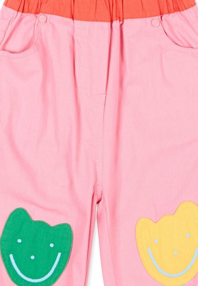 Pantalon rose pour enfants avec une ceinture élastique orange et des patchs souriants verts et jaunes sur chaque genou.