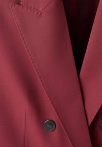 Dvouvrstvý bordó blejzr s ostrými klopami, zapínáním na knoflíky a hladkou texturou látky s jemným prošíváním.