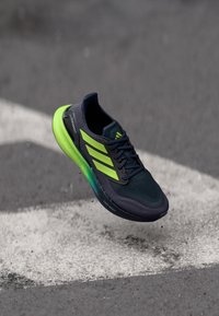 Chaussure de sport avec un dessus bleu marine, des accents vert fluo et un maillage texturé. Caractérisée par une semelle épaisse vert clair avec l'étiquette "Light Boost".