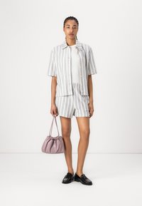 Tekstured lett skjorte med blå striper, sammen med matchende shorts. Holder en liten rosa veske. Svarte loafers fullfører antrekket.