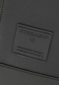 Materiale in pelle nera con una superficie testurizzata, dotato di un'etichetta loggata in rilievo rettangolare con "STRELLSON" e coordinate.