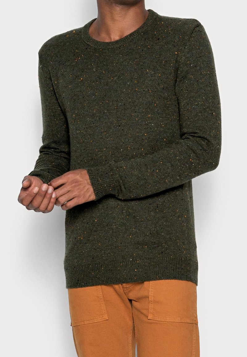 Pull vert à texture côtelée, col rond et éclats de couleurs. Associé à un pantalon cargo orange, mettant en avant des manches longues et une coupe ajustée.