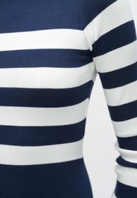 Πουλόβερ με λωρίδες σε ναυτικό μπλε και λευκό, με ριμπ υφή, εφαρμοστό σχέδιο και μακριά μανίκια. Οι λωρίδες έχουν ομοιόμορφο και συνεπή πλάτος.