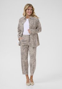 Conjunto de blazer y pantalones de estampado de leopardo beige, con un corte relajado, dos bolsillos laterales y una textura suave. Se lleva con una blusa blanca y zapatos claros.
