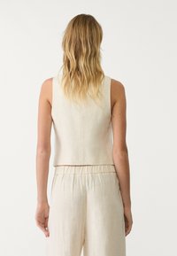 Haut court beige à coupe droite, en tissu texturé, avec une encolure lisse et une taille froncée.