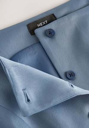 Sacou bleu deschis cu o textură fină, prevăzut cu trei nasturi albastru închis și o etichetă inscripționată „NEXT”. Include o căptușeală de culoare albastru contrastantă.