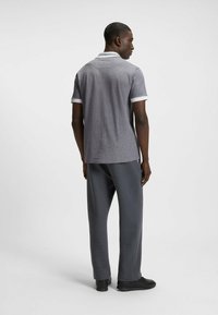 Harmaa polo-paita, jossa on teksturoitu kuvio, valkoinen kaulus ja hihansuut; yhdistettynä harmaisiin housuihin ja mustiin kenkiin. Näkymä takaa.