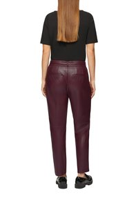 Bordeaux leren broek met een slim fit, voorzien van achterzakken en een gladde textuur. Gepaard met zwarte schoenen en een zwart topje.