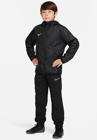 Veste de sport noire Nike avec capuche, poignets élastiques et fermeture éclair, associée à un pantalon de jogging assorti, arborant le logo Nike en blanc.