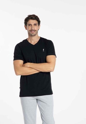 T-shirt noir à col en V avec des manches courtes, texture lisse, et un petit logo sur la poitrine gauche ; associé à un pantalon gris clair.