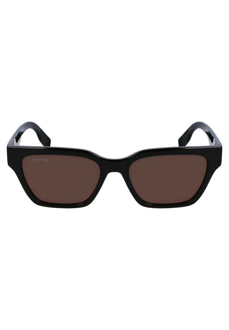 Lunettes de soleil noires de forme géométrique, avec des verres brun foncé et une finition brillante. Présente le logo Lacoste sur la branche gauche.