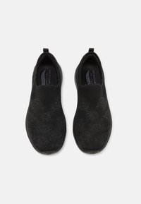 Fekete slip-on cipők struktúrált kötött felsőrésszel, elasztikus gallérral és gumitalppal, diszkrét mintákkal és párnázott talpbetéttel.