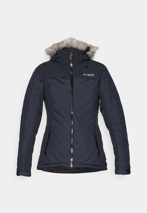 Navy blue insulated jacket with a fur-lined hood, featuring a front zipper, two side pockets, and a chevron pattern on the fabric.