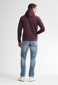 Bordeauxroter Kapuzenpullover mit lockerer Passform, kombiniert mit hellblauen Jeans und weißen Sneakern. Glattes Material mit gerippten Bündchen.