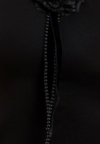 Sort stof prydet med en tekstureret blomst, der har en lodret række af skinnende sorte perler og et velourbånd som accent.