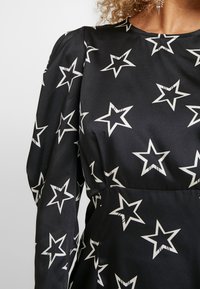 Svart klänning i slät tyg med ett mönster av vita stjärnor över hela, med puffärmar och rund halsringning.