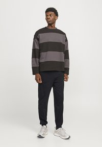 Zwart en grijs gestreepte sweatshirt met een relaxte pasvorm, gecombineerd met marineblauwe joggerpants en grijze sportschoenen. Vlakke katoenen textuur.