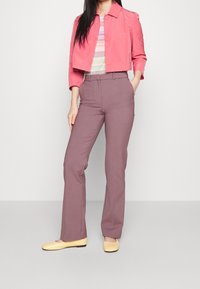 Roze cropped jas, gemêleerd topje, lavendel wijd uitlopende broek en gele platte schoenen. Gladde stoffen, nauwsluitende pasvorm en knoopdetails op de jas.