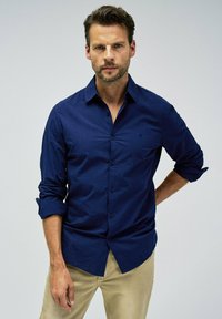 Camisa de hombre azul marino de botón en tejido texturizado; presenta un cuello clásico, mangas largas y un pequeño logo en el pecho.