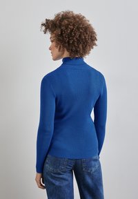 Räfflad blå turtlenecktröja i stickat tyg, med en åtsittande design, långa ärmar och hög krage. Jeansen i denim syns nedanför.