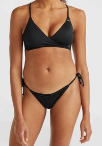 Set di bikini nero con top triangolare dotato di spalline sottili e design avvolgente, e slip con lacci laterali. Texture liscia e stile minimalista.